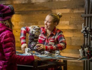 Young woman renting skis and ski boots while ski technician tuning the ski gear.