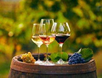 three wine glasses with different wines in each one, set on top of a barrel 
