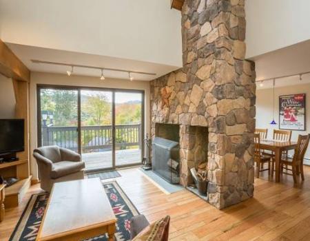 an open-concept living space, with a stone fireplace separating it from the dining room inside a killington townhome
