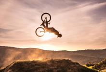 Shadowed person doing a flip on a mountain bike with sunset in background