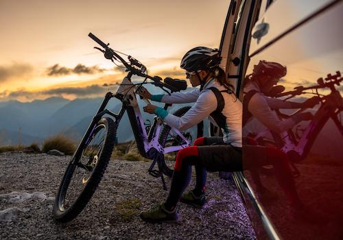 female cyclist with a bike on a mountain at sunset