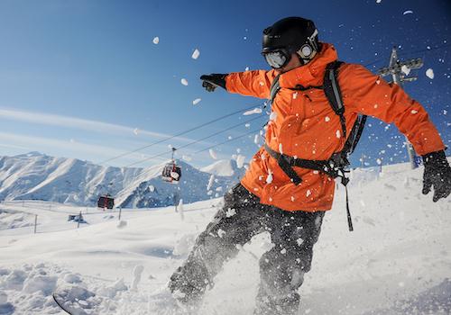snowboarder in bright orange jacket riding down a mountain slope