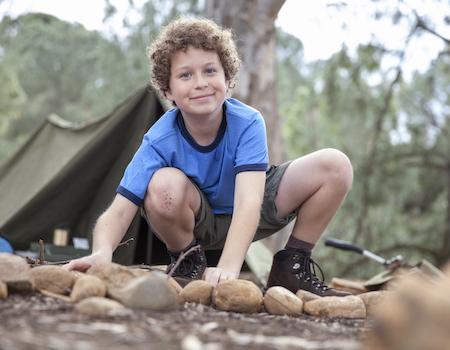 Young boy by a camp fire with a tent in the background